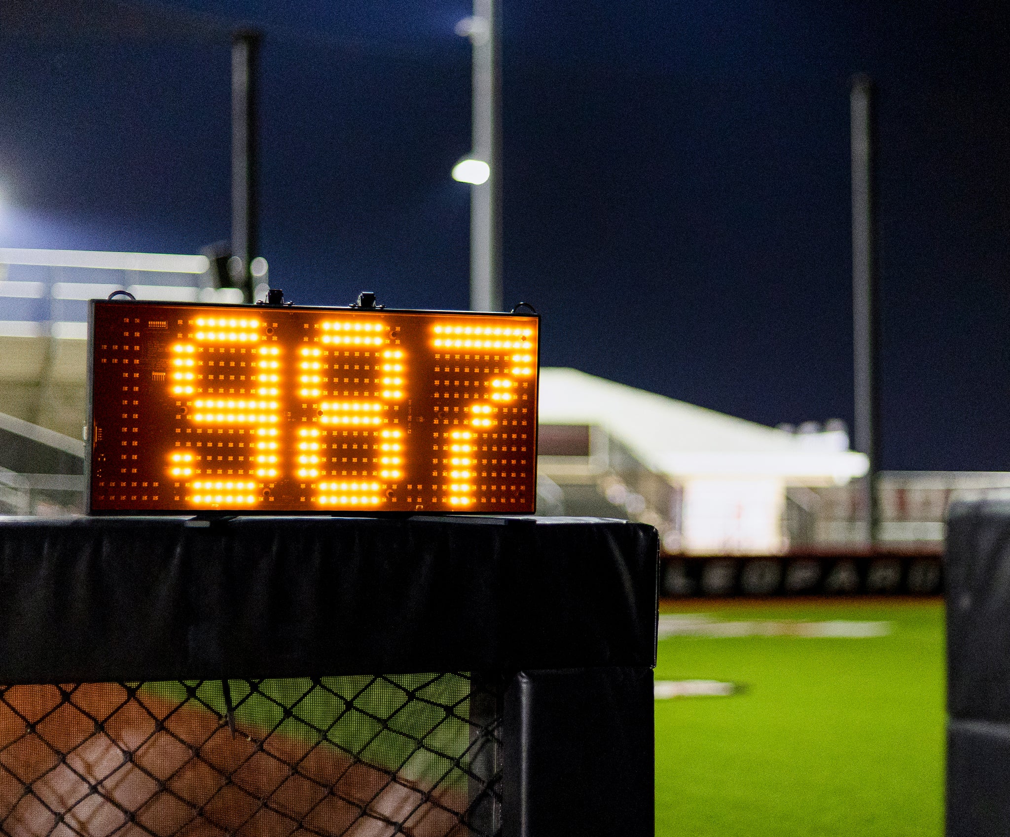 A Stalker Sport 3.5 Digit LED Speed Sign sitting on top of a wall at a baseball field. It shows a speed of 98.7