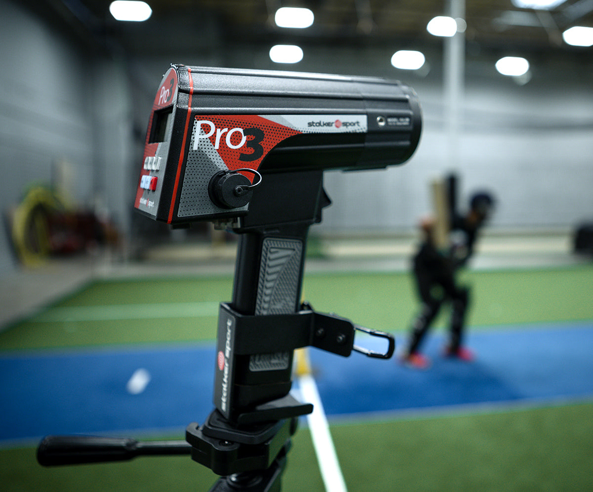 A Stalker Sport Pro 3s handheld sports radar gun in a tripod mount at a cricket training facility measuring velocities.