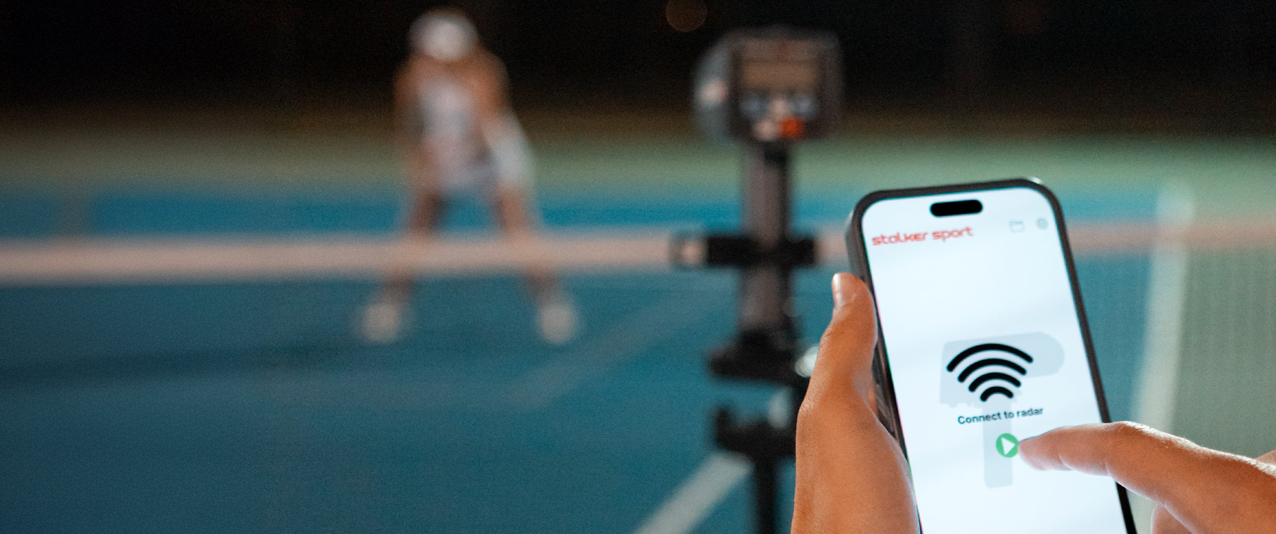 A person holding a phone using the Stalker Sport Radar app on the connection screen, pushing the green connect button. A Sport 3 Connect radar and tennis player are in the background.
