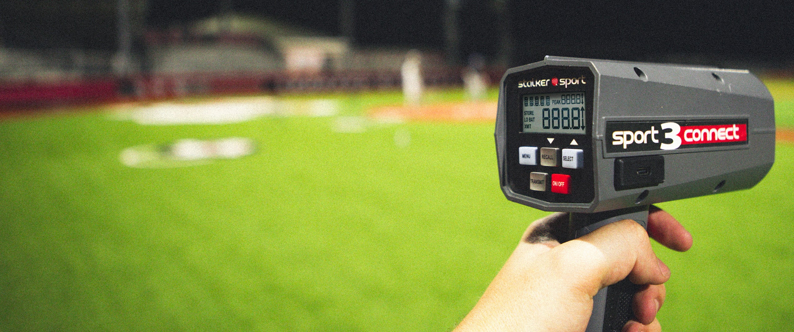 A hand holding a Sport 3 Connect radar with a baseball field in the background.