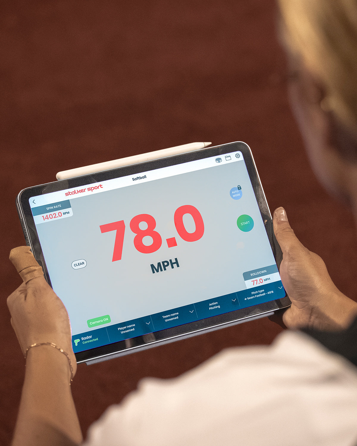 An over-the-shoulder view of a woman holding an iPad running the Stalker Sport Radar App showing a velocity of 78.0 MPH.