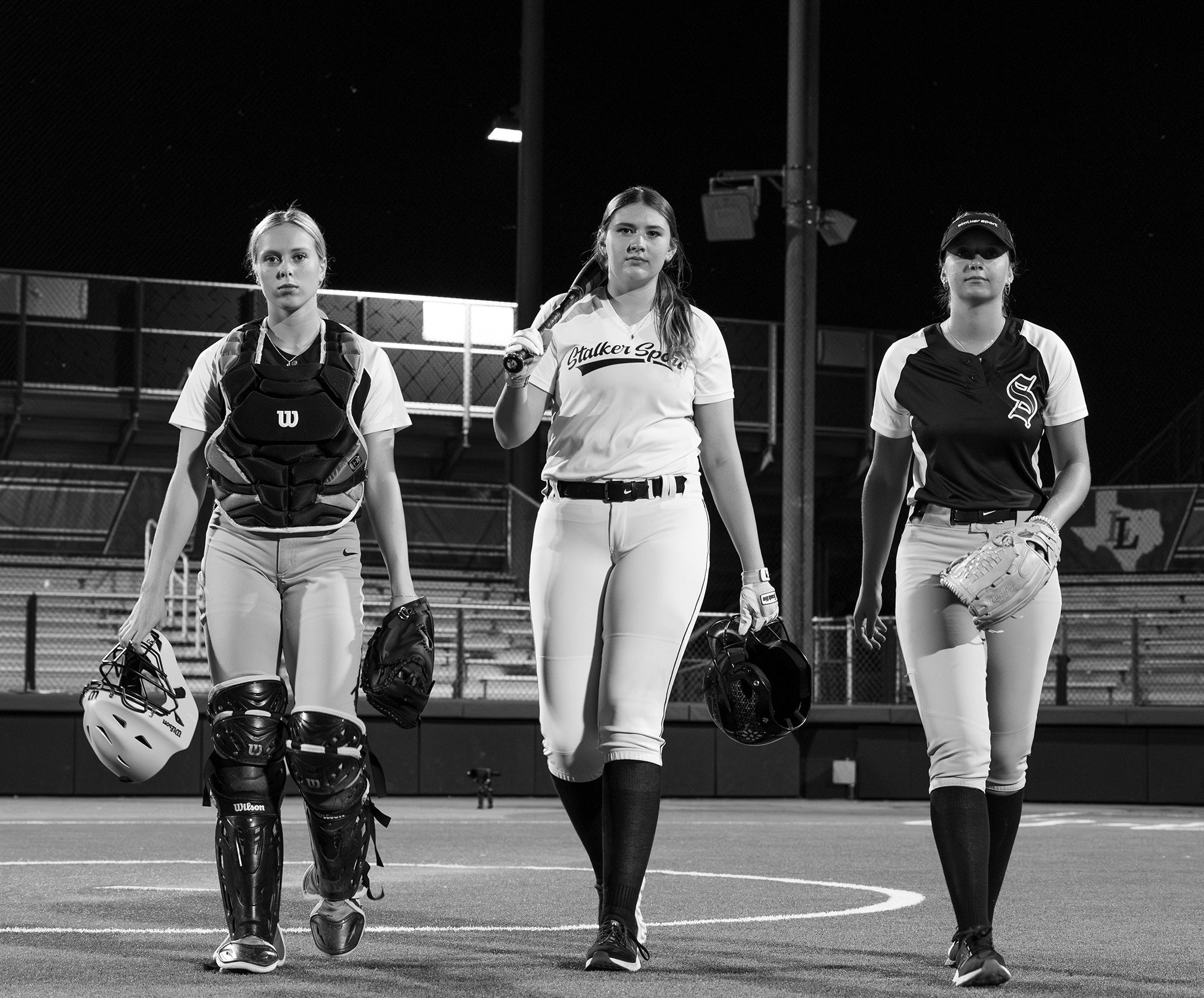 Three women from Team Stalker Sport Softball walking towards the camera with their gear.