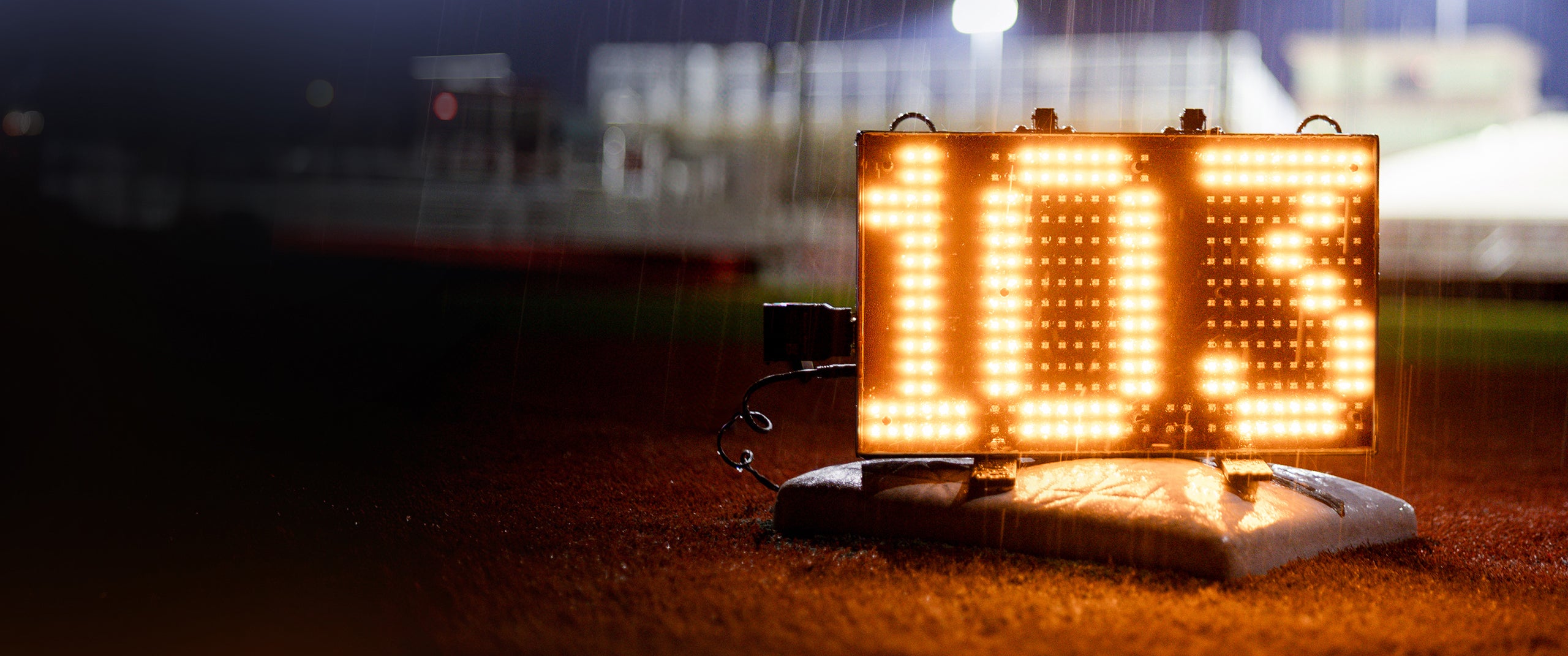 A Stalker Sport 2.5 digit LED Speed Sign on a base in a baseball field in the rain.