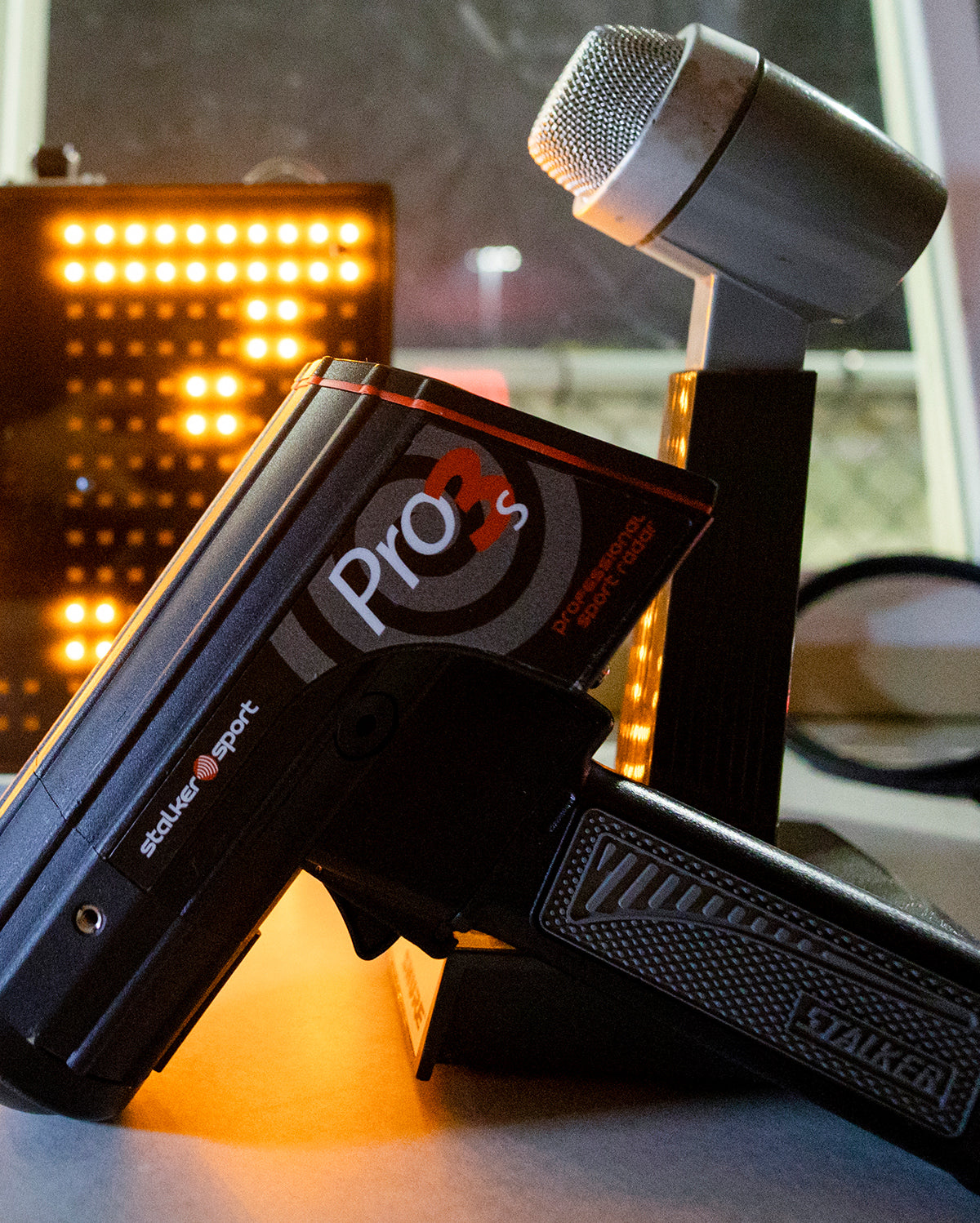A close up of the Stalker Sport Pro 3s radar placed on the counter of the press box of a baseball field, with a microphone and LED speed sign in the background. 