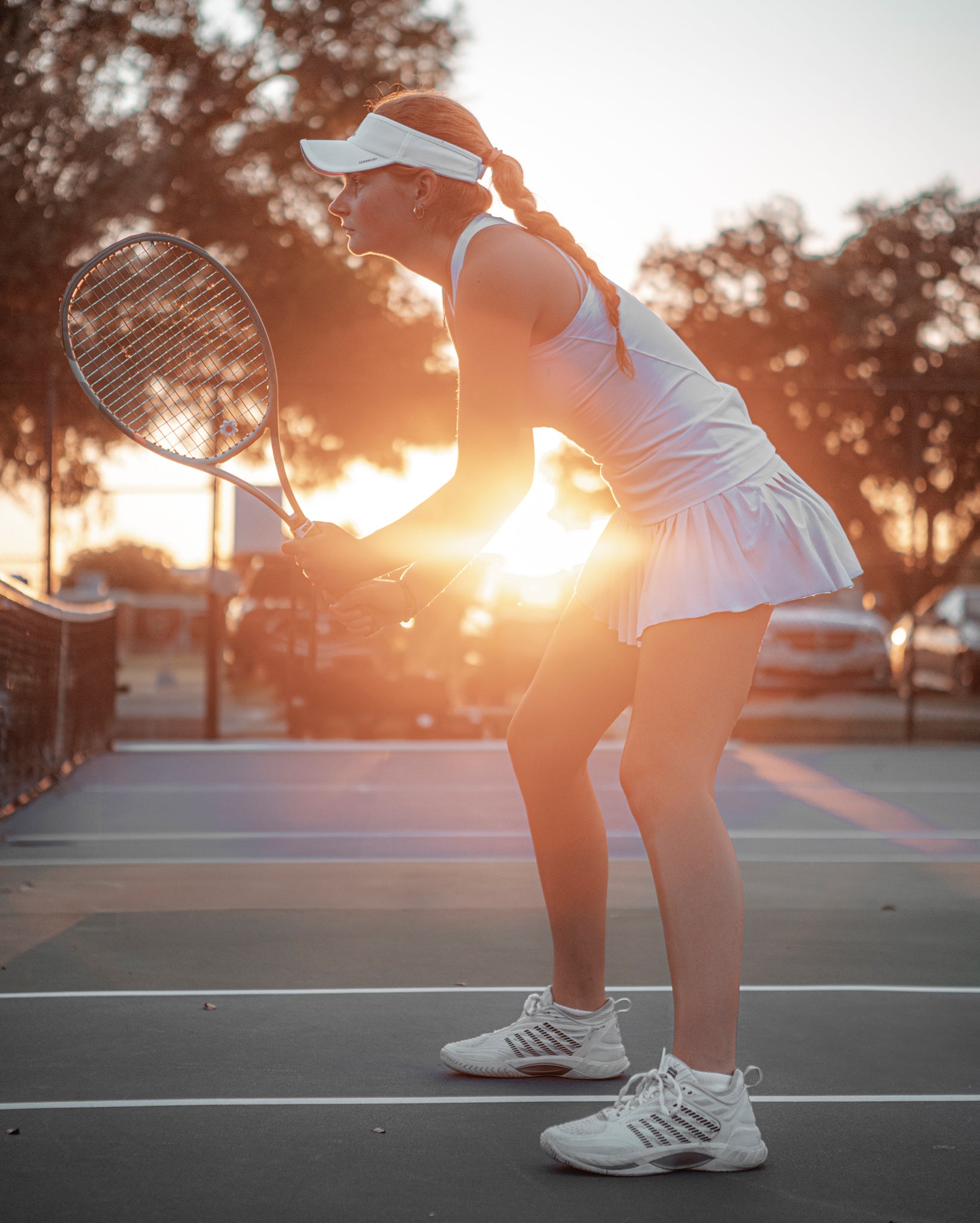 A woman playing tennis for Team Stalker Sport ready to return a volley on a tennis court during sunset.