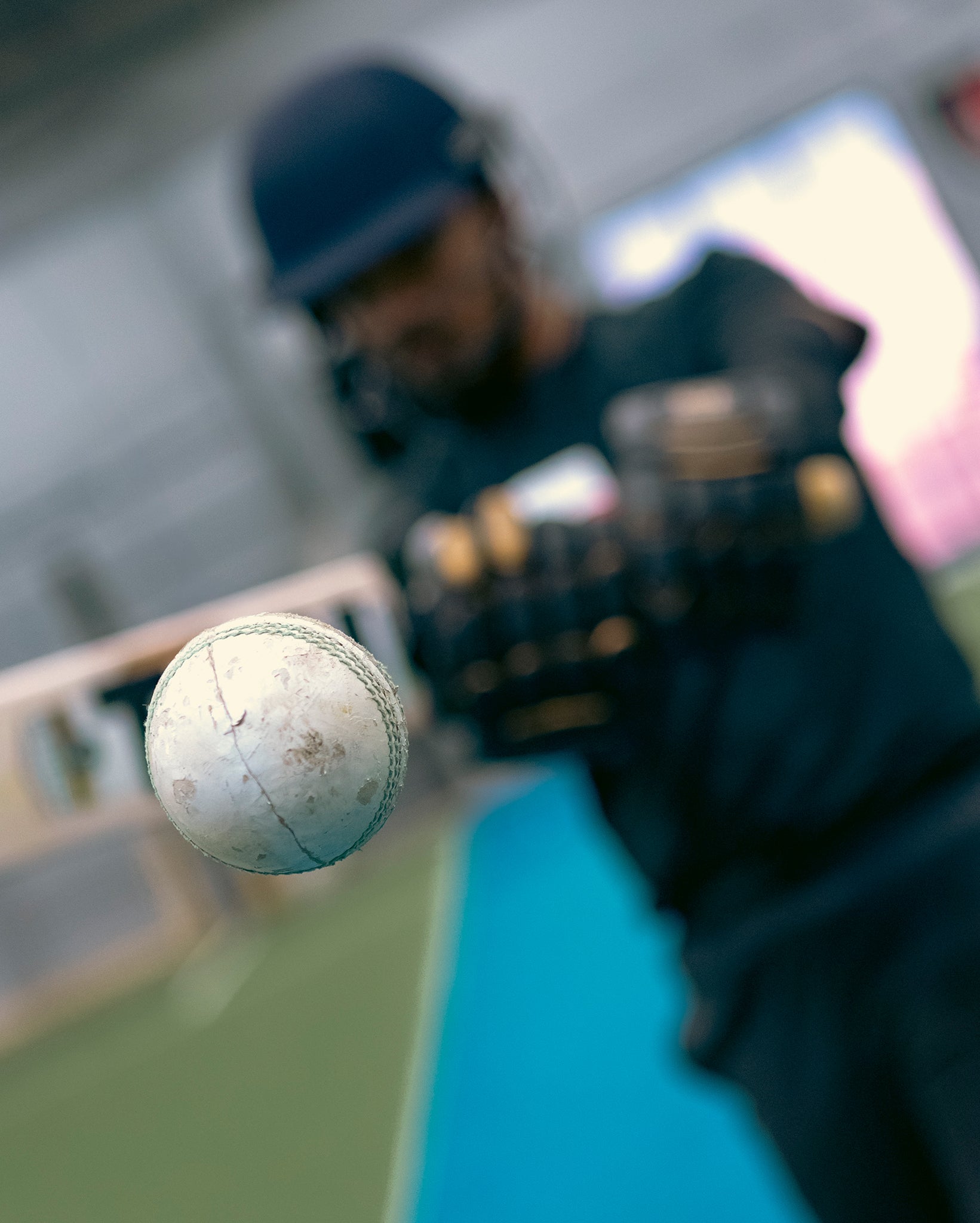 Close-up of a cricket ball with a blurred background of a cricket player on Team Stalker Sport holding a bat.