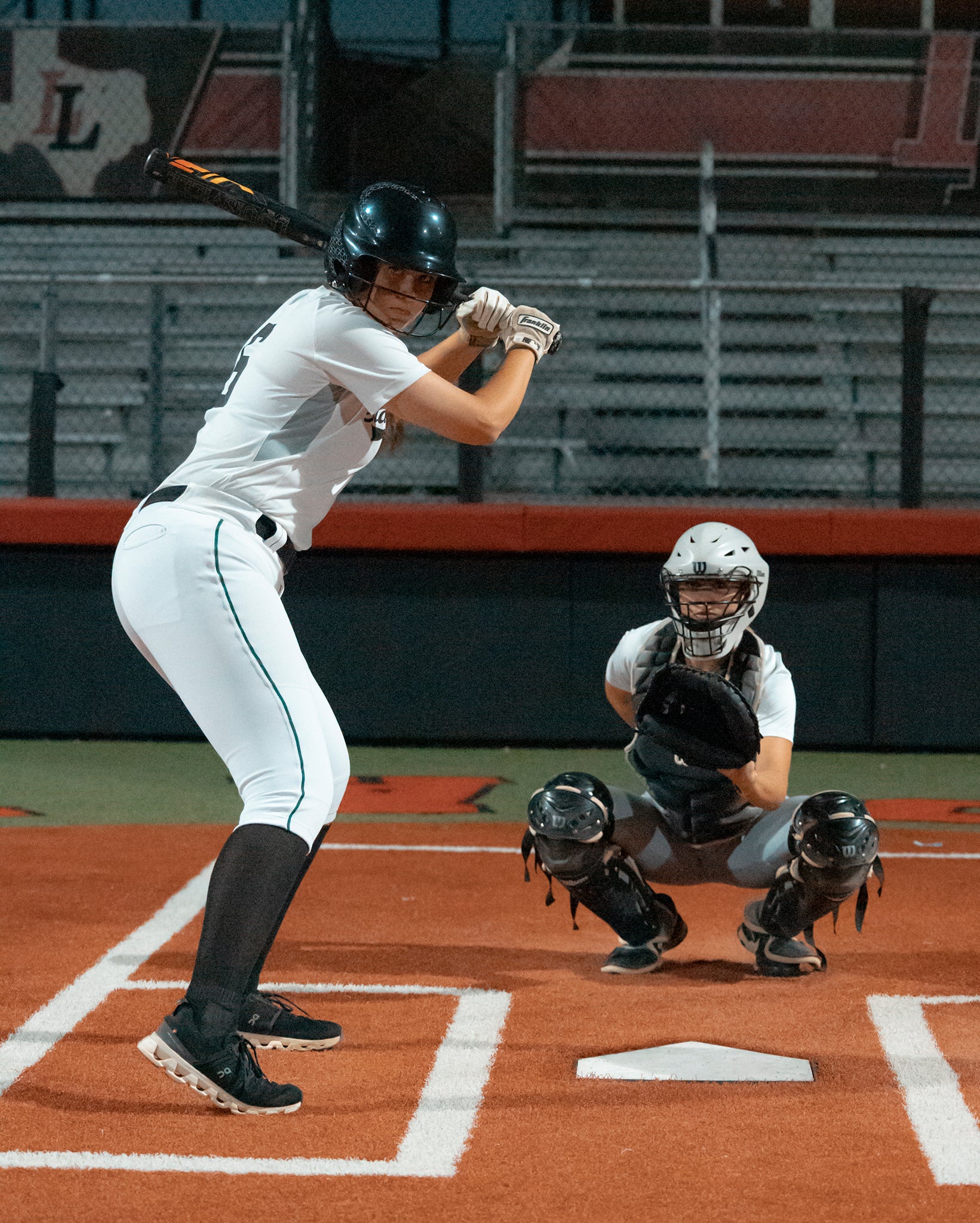 A woman from Team Stalker Sport playing softball ready to bat with a catcher crouching behind her.