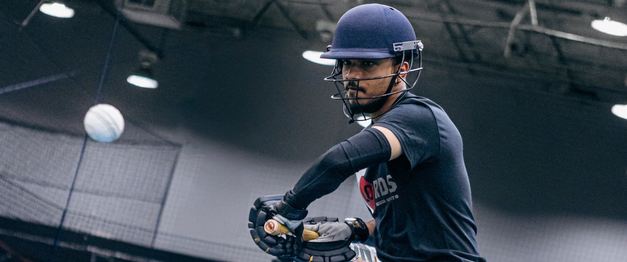 A cricket player hitting a ball in a training facility.