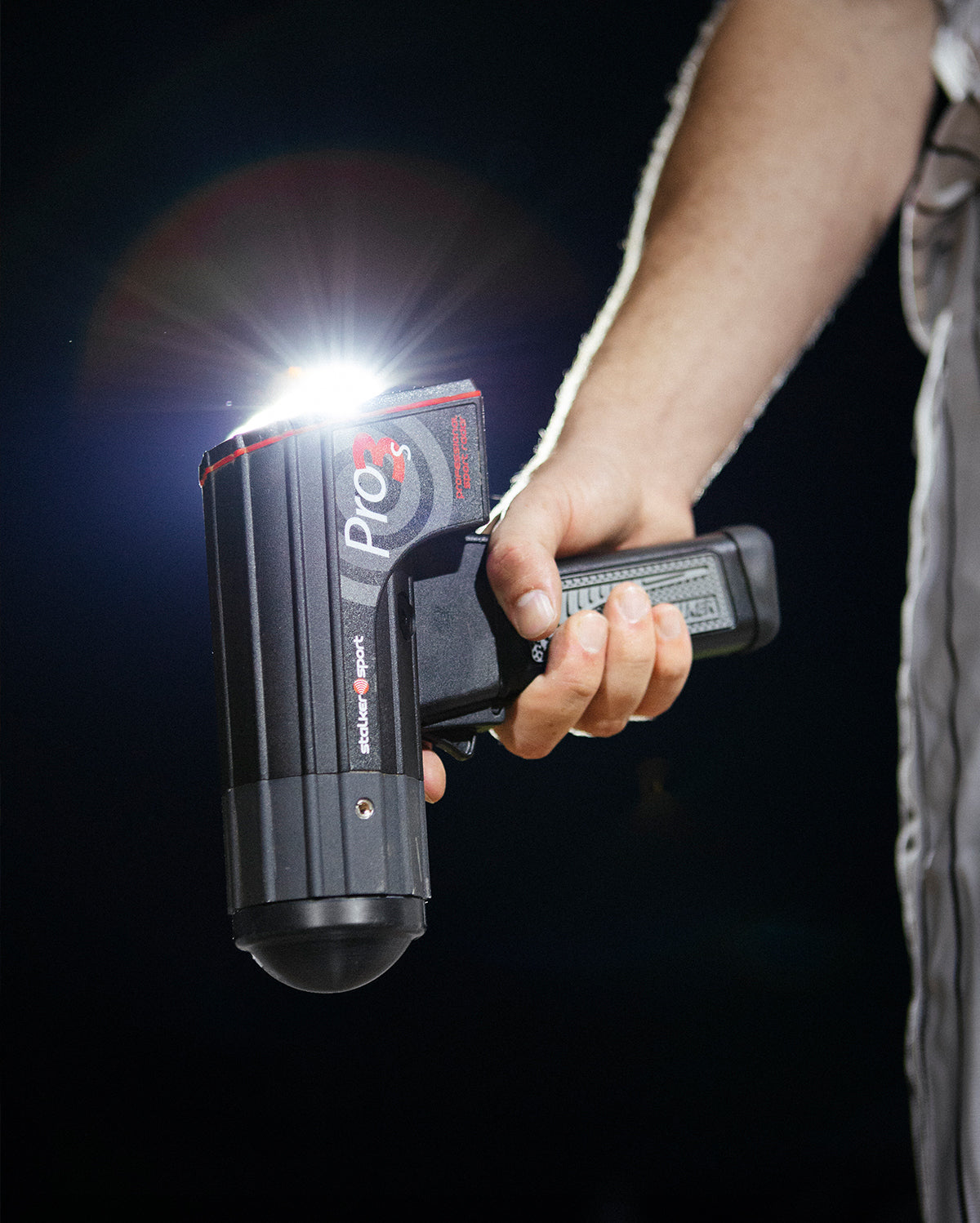 A baseball player holding a Stalker Sport Pro 3s radar gun at night.