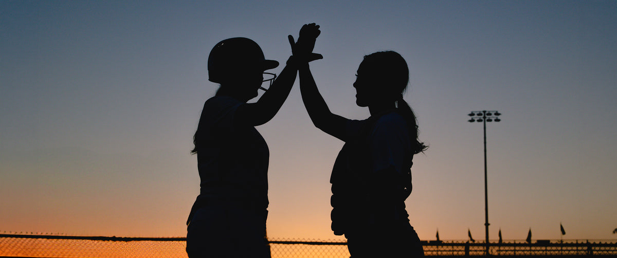 two softball players high-fiving out on the softball field