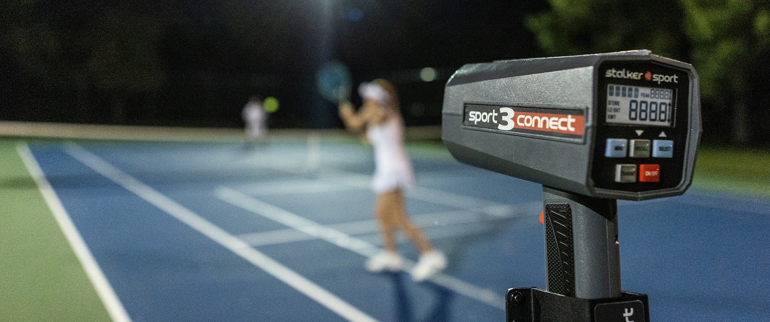 A Stalker Sport 3 Connect on a tripod in the foreground with an out-of-focus tennis game happening in the background. 