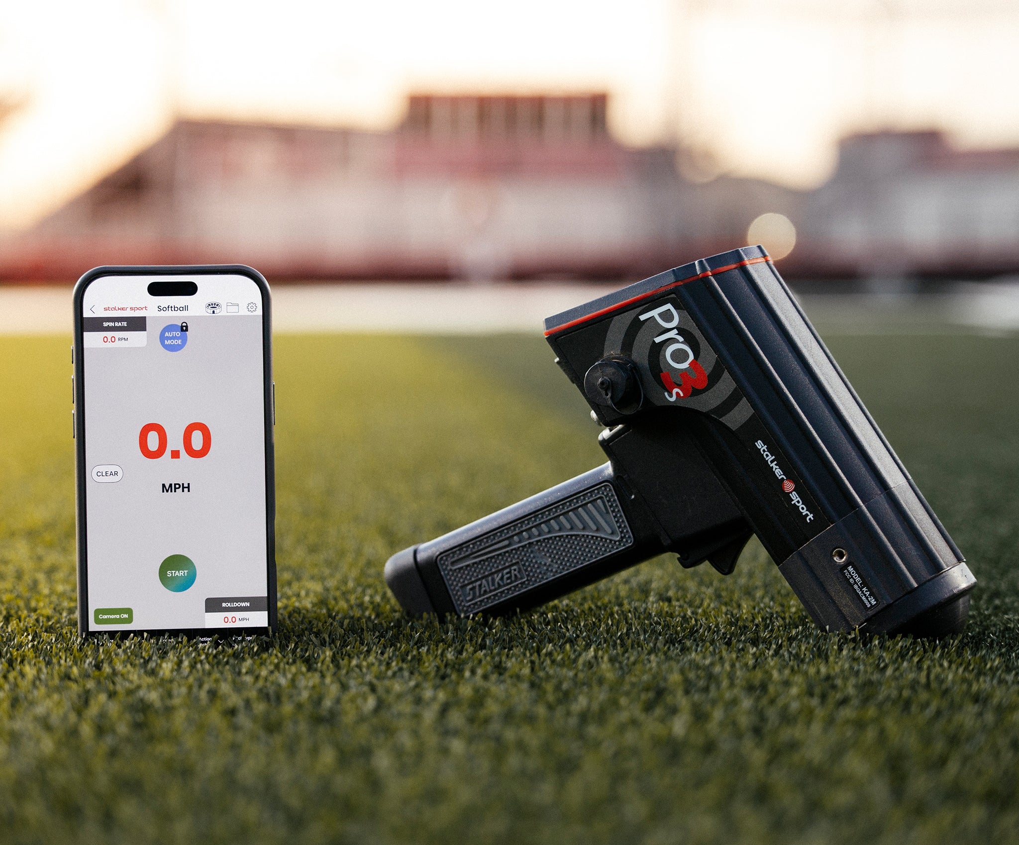 An iPhone displaying the Stalker Sport Radar app next to a Pro 3s radar gun on a baseball field. 